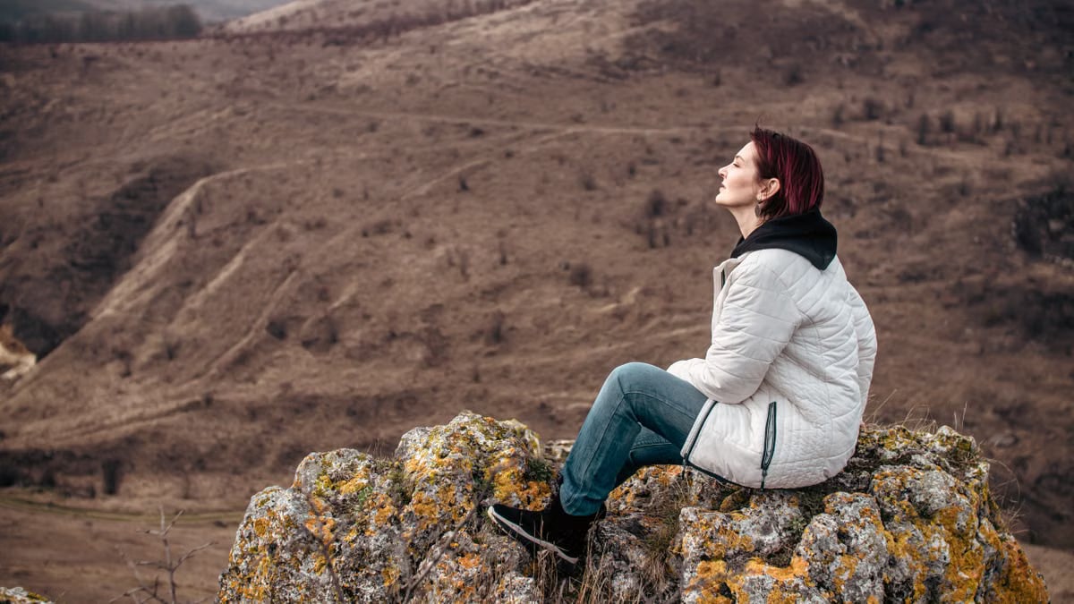 Woman enjoying solitude on a rocky mountain peak, eyes closed in leisure.